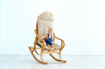 Little girl rides a rocking chair on the background of a white b