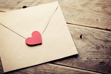 Envelope or letter and red heart on rustic wooden table for love message on Valentines Day in retro toning.