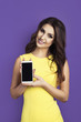 Beautiful smiling woman shows phone black screen. Device mockup between female hands. Studio shot purple background yellow dress.