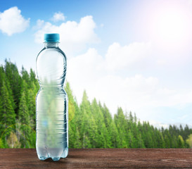 Wall Mural - Bottle of clear water on wooden table against nature background