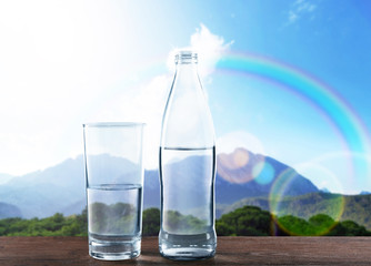 Wall Mural - Bottle and glass of clear water on wooden table against nature background