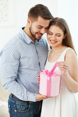 Wall Mural - Cute young couple with giftbox at home