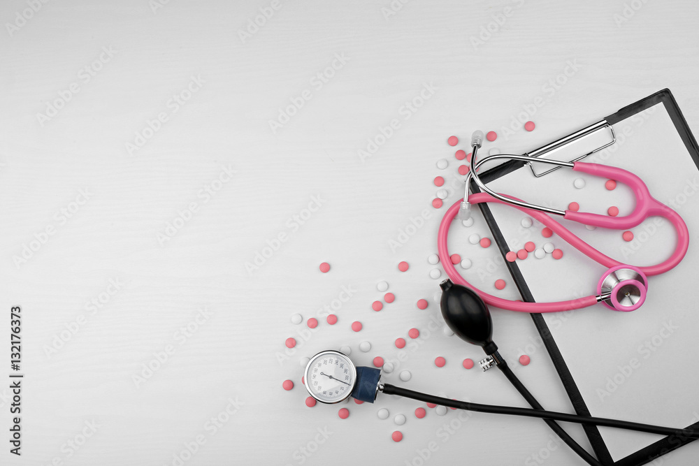 Stethoscope with clipboard and pills on white background