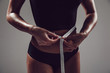 © kanashkin - Athletic slim woman measuring her waist by measure tape on grey background