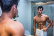 © theartofphoto - Shirtless muscular handsome young man looking at himself in bathroom mirror in the morning