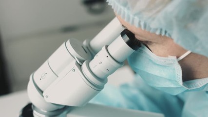 Wall Mural - middle age female scientist in uniform and medical face mask doing microscopic examination in labora