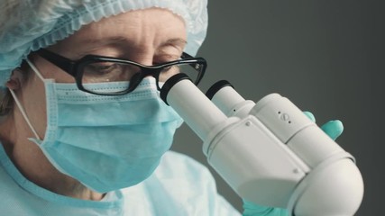 Wall Mural - middle age female scientist in uniform and medical face mask doing microscopic examination in labora