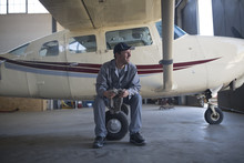 Mechanic Sitting Next To Light Aircraft In Airfield Hangar