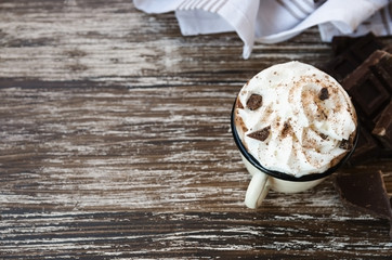 vintage mug of hot chocolate cocoa with whipped cream and slice of bitter chocolate on wooden backgr