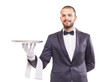 Waiter in tuxedo and gloves holding empty tray and napkin over w