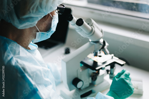 Fotografía Scientist in blue medical gloves and uniform learning samples with microscope in laboratory