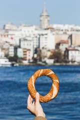 Wall Mural - Woman hand holding a traditional Turkish simit on sea background