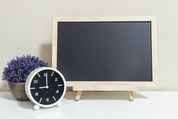 Closeup alarm clock for decorate show 9 o'clock with wood black board on white wood desk and cream wallpaper textured background , selective focus at the clock