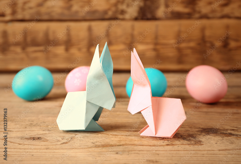 Origami bunnies and Easter eggs on wooden background