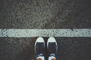 Male feet in white socks and gumshoes standing near grunge white line on gray asphalted road, ready to go