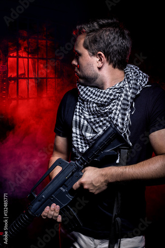 Fotografia, Obraz Soldier with a gun surviving in the smoky ruins of an urban warzone on fire