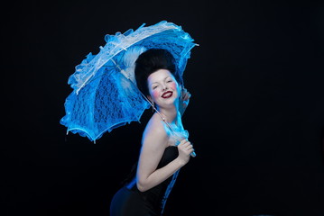 emotional actress brunette woman in an ancient medieval attire and lush hair with white feathers with a white lace umbrella in hand on a black background in the studio