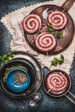 Raw Sausage On Vintage Cutting Board With Herbs And Spices, Preparation On Dark Rustic Kitchen Table, Top View