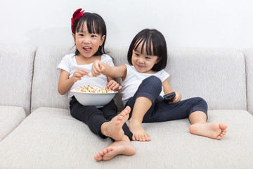 Wall Mural - Happy Asian Chinese little sisters eating popcorn on the sofa