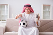 © Elnur - Young arab man watching football sitting on sofa