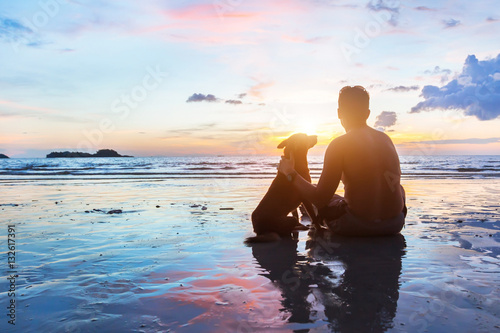 Fotografía friendship concept, man and dog sitting together on the beach at sunset