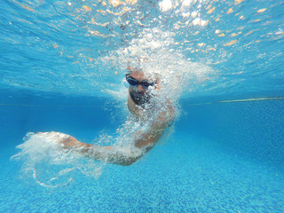 Beard man with glasses swimming under water in the pool