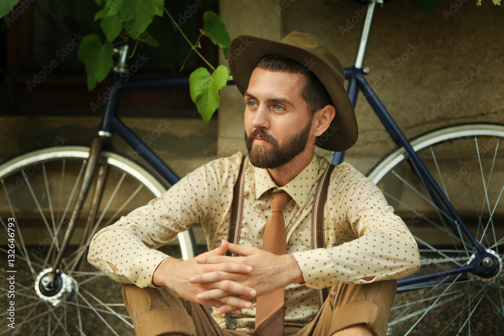 Stylish man with bicycle sitting on street