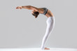 © fizkes - Young attractive woman practicing yoga, doing Standing Backward Bend exercise, Ardha Chakrasana pose, working out wearing sportswear, indoor full length, isolated, grey studio background