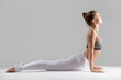 © fizkes - Young attractive woman practicing yoga, stretching in Cobra exercise, Bhujangasana pose, working out wearing sportswear, indoor full length, isolated against grey studio background
