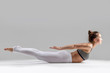 © fizkes - Young attractive woman practicing yoga, stretching in Double Leg Kicks exercise, Salabhasana pose, working out wearing sportswear, white pants, indoor full length, isolated, grey studio background