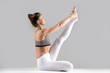 © fizkes - Young attractive woman practicing yoga, sitting in Heron exercise, Krounchasana pose, working out wearing sportswear, white pants, bra, indoor full length, isolated against grey studio background