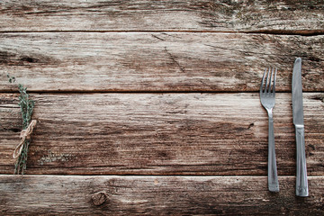 Rustic wooden table with knife and fork free space. Top view on grunge rural background with cutlery and herbs, background for meal advertisement or restaurant menu