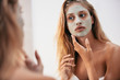 Woman looking in the mirror with face mask