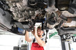 © industrieblick - Automechaniker repariert defektes Fahrzeug auf der Hebebühne in einer Werkstatt