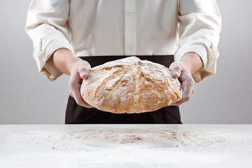 Baker man holding rustic organic loaf of bread in hands