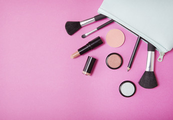 Wall Mural - Make up products spilling out of a blue cosmetics bag on to a bright pink background with empty space at side