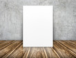 Blank white paper poster leaning at concrete wall on wooden floo