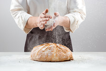 The male hands in flour and rustic organic loaf of bread