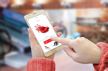 Poster - Shopping web site app on smart phone. Woman holding mobile device and buy red shoes. City shopping center in background.