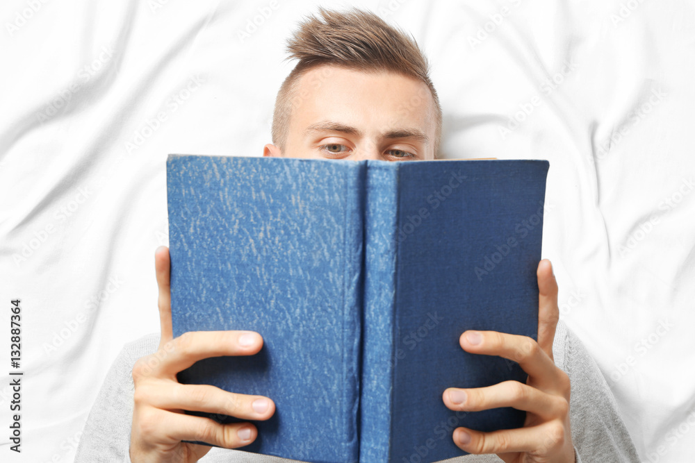 Young man reading book while lying on bed