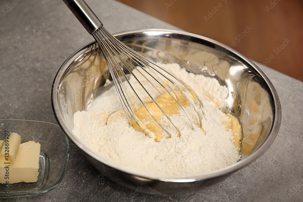 Bowl with flour, dough and whisk on kitchen table, closeup