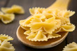 Raw farfalle or bow-tie pasta on wooden spoon, photographed with natural light (Selective Focus, Focus on the middle of the upper pasta on the spoon)