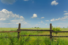Country Timber Fence. Old Wood Fence With A Green Country Field Behind It. Wooden Slit Rail Fence Fades Into The Distance Across A Green Field Blue Sky And White Clouds Above.