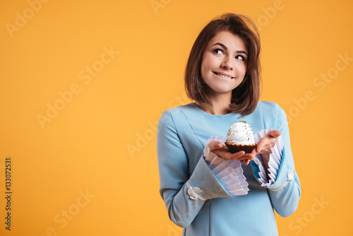 Fotografía Pensive smiling young woman holding cupcake and thinnking