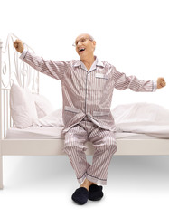 Canvas Print - Elderly man in pajamas sitting on a bed and yawning