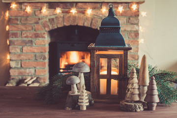 Wall Mural - Winter setting: lantern and handmade wooden toys in front of fireplace with burning logs, decorated fireplace, selective focus; dark vintage style toned photo