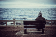 Man Sitting On Bench Overlooking Sea