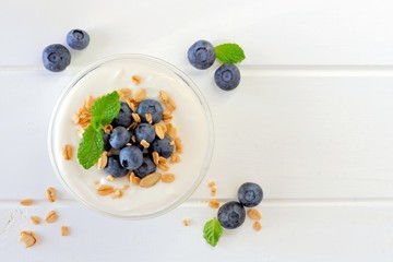 Wall Mural - greek yogurt with blueberries and granola, above view on white wood