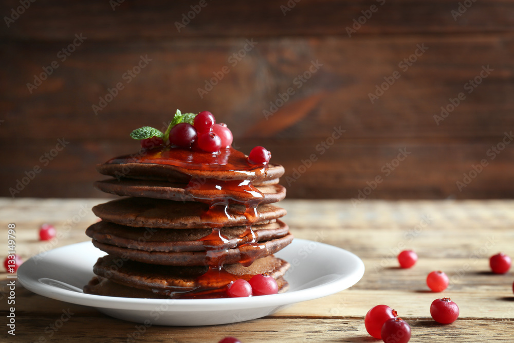 Plate with delicious chocolate pancakes and berries on wooden table