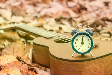 Wall Mural - Retro Alarm on Ukulele Guitar on Autumn Leaves Background. Time